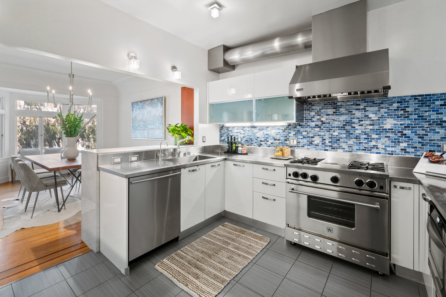 Property Photo: Kitchen has darker gray large tile floor with all white cabinetry. Counter tops are stainless steel. 