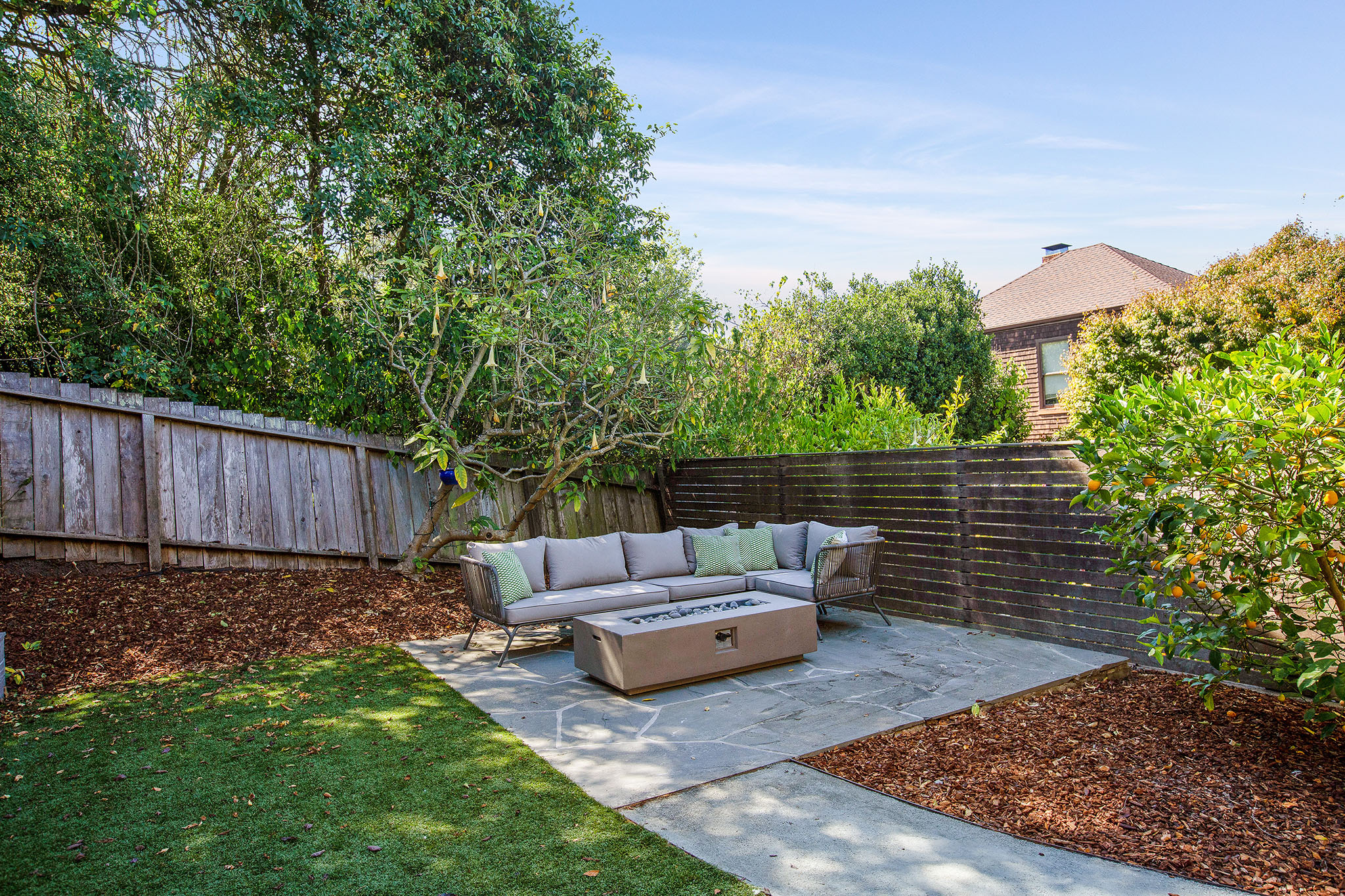 Property Photo: Back yard has cement pathway to sitting area. There are wood chip planter beds and a grass yard area. 