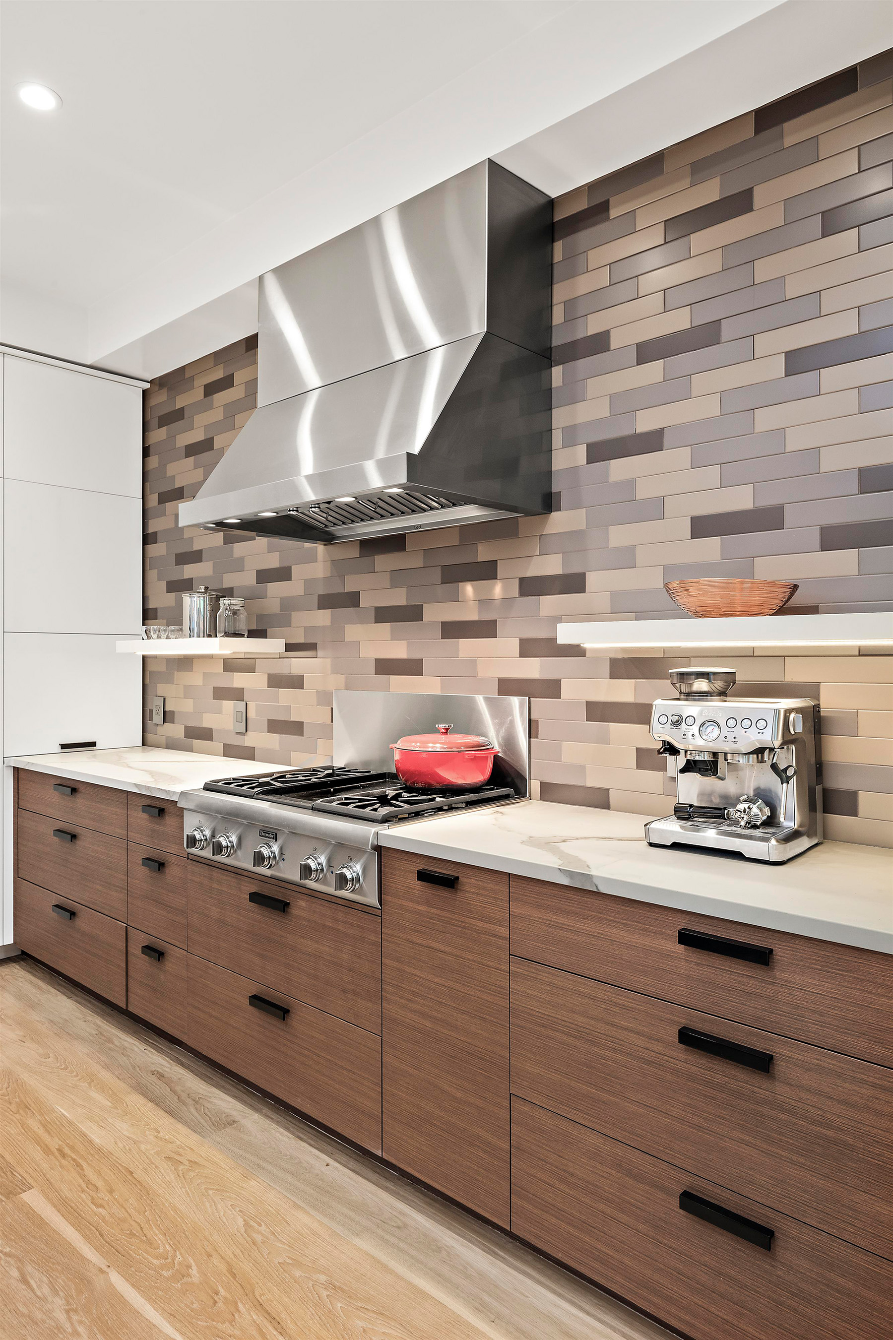 Property Photo: Gas stove is centered on back wall with with large stainless hood and tile backsplash detail. 
