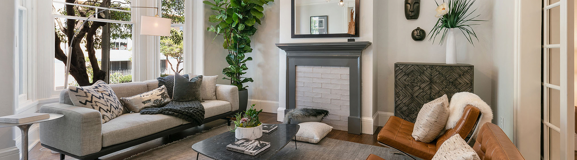 A living room with large white framed windows, a grey couch, and fireplace