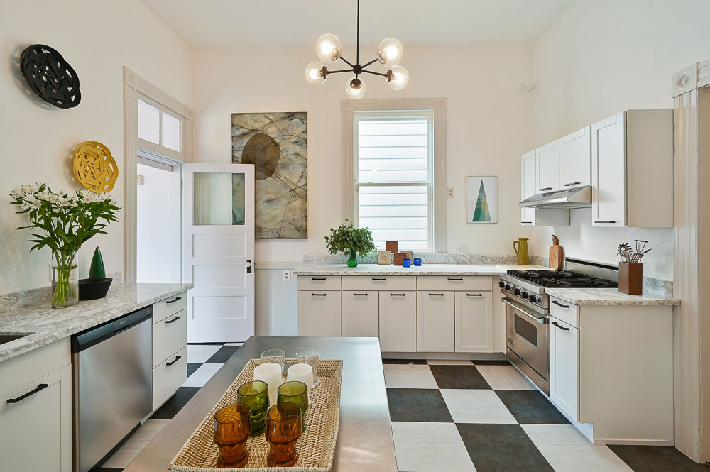 Property Photo: View of the kitchen, featuring large black and white tile flooring and white cabinets