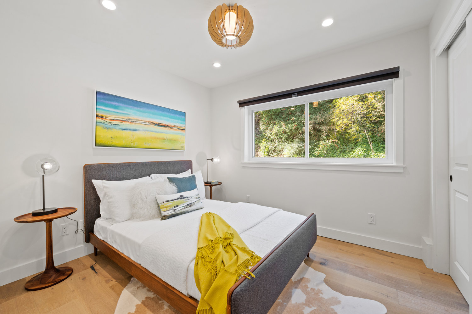 Property Photo: Bedroom three, featuring a large window, mid-century light fixture, and wood floors