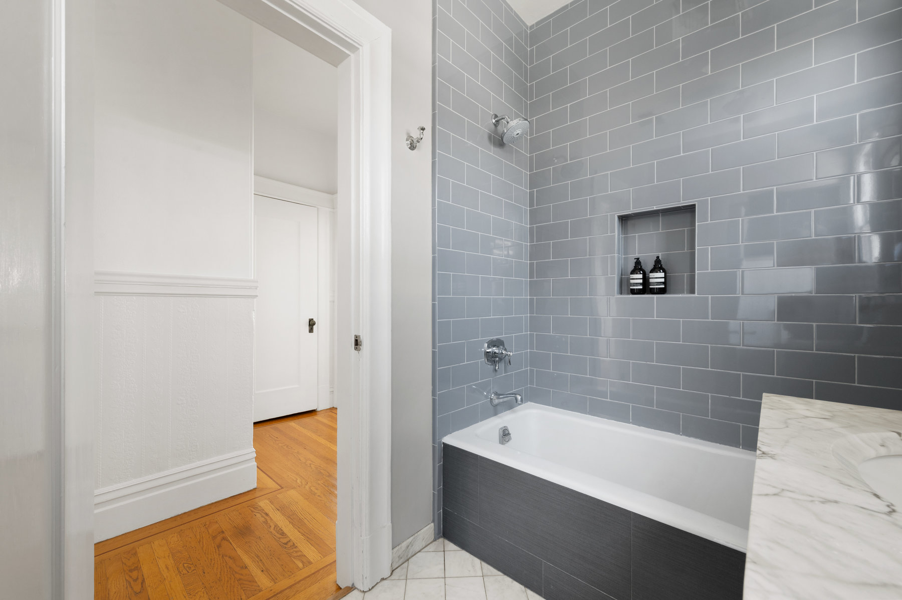 Property Photo: There is grey tile detail surrounding tub, and white tile floors. Bathroom has been updated. 