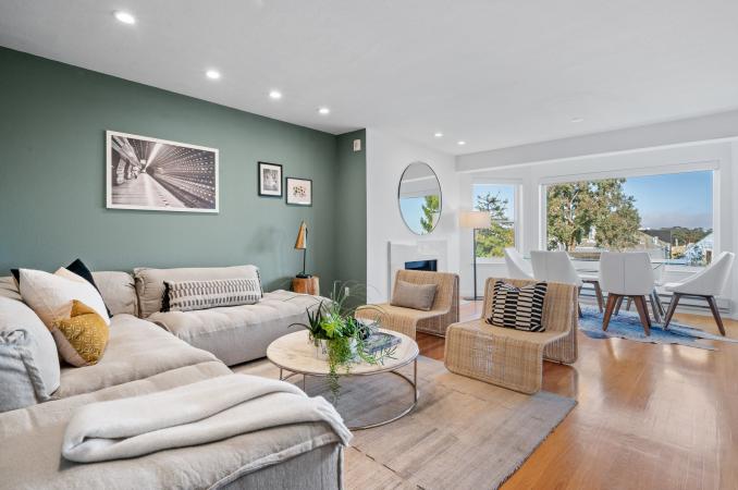 Property Thumbnail: Living/dining space of 222 Parnassus Unit E. Open concept w/ large L shaped couch and dining table in front of windows looking out to backyard. 