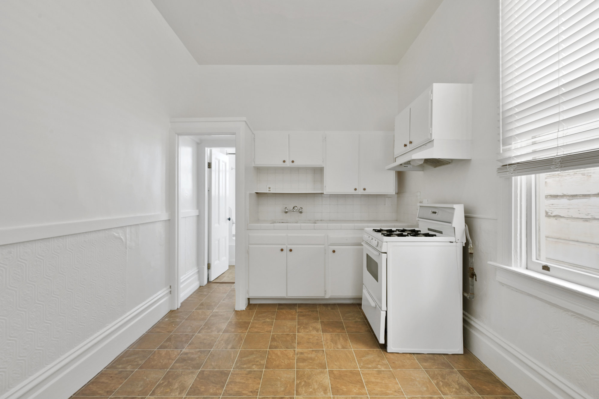 Property Photo: Kitchen with white cabinets, showing a stove and window